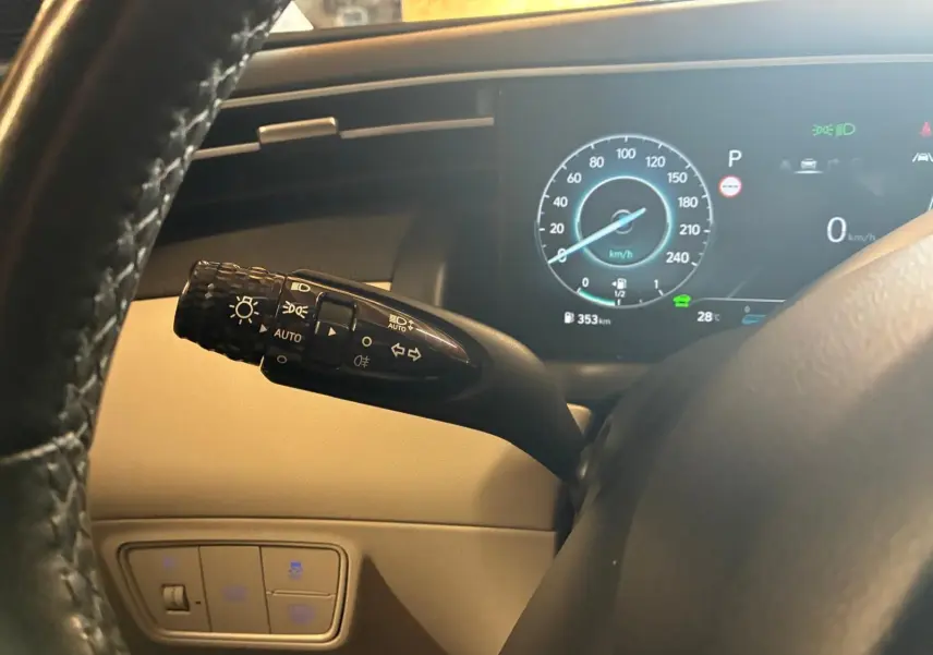 Gros plan sur la manette des phares à gauche du volant dans l’habitacle beige du Hyundai Tucson noir, tableau de bord digital visible.