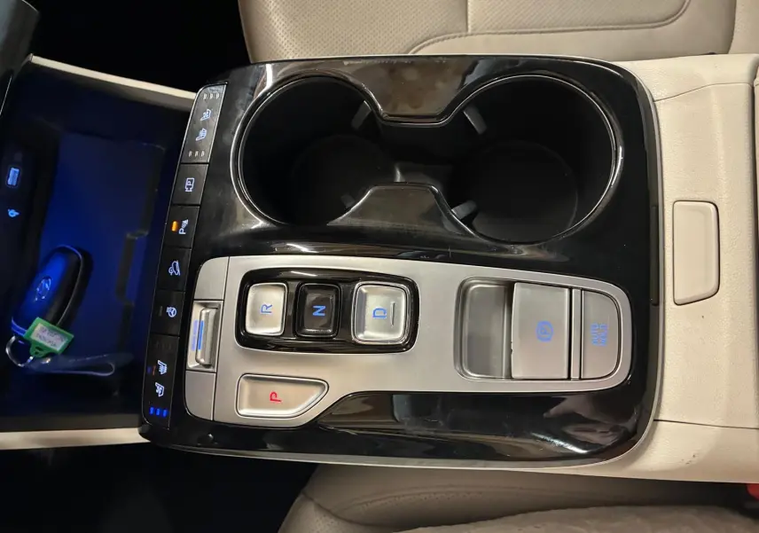 Vue rapprochée de la console centrale beige du Hyundai Tucson 2022, avec commandes de boîte auto et porte-gobelets noirs.