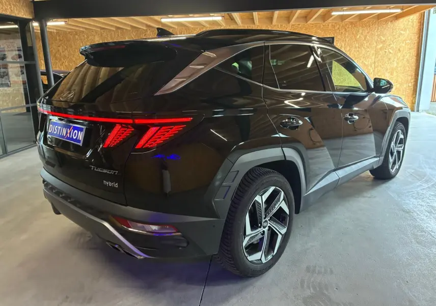 Vue 3/4 arrière droite d'un Hyundai Tucson noir hybride 2022 avec feux arrière LED distinctifs et jantes modernes.