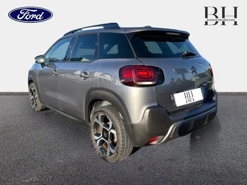 Vue 3/4 arrière droit d'un Citroën C3 Aircross gris acier avec barres de toit et jantes diamantées noires.