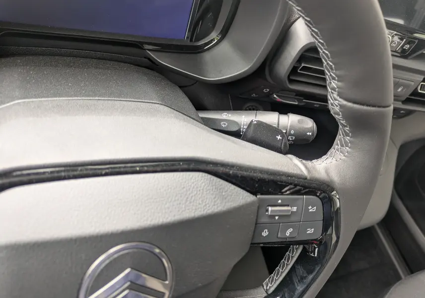 Gros plan sur le volant noir avec surpiqûres blanches du Citroën Berlingo 2025, montrant les commandes intégrées côté droit.
