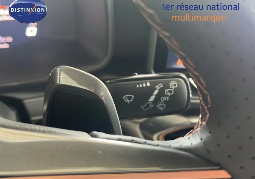 Gros plan sur la palette de changement de vitesse et le commodo d’essuie-glace, volant cuir perforé brun visible.