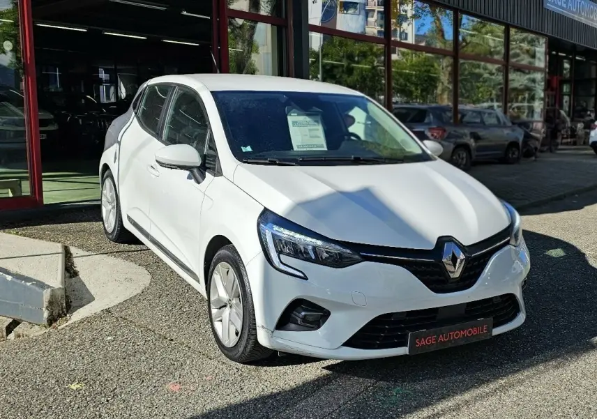 Renault Clio blanche glacier vue 3/4 avant droit, garée devant un showroom avec plaque Sage Automobile.