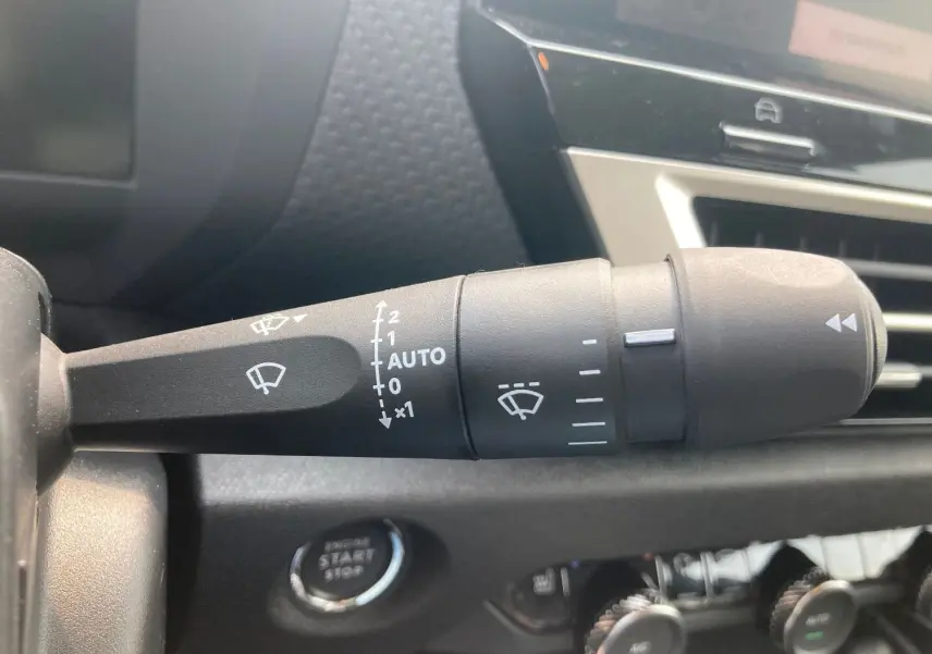 Gros plan sur la commande d'essuie-glace à gauche du volant dans l'habitacle noir de la Citroën C4 Facelift Hybrid 2025.