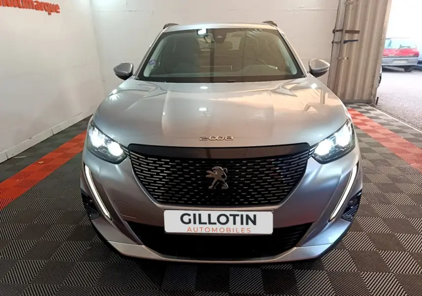Vue frontale d'un Peugeot 2008 gris clair avec phares allumés et calandre noire au logo lion visible.