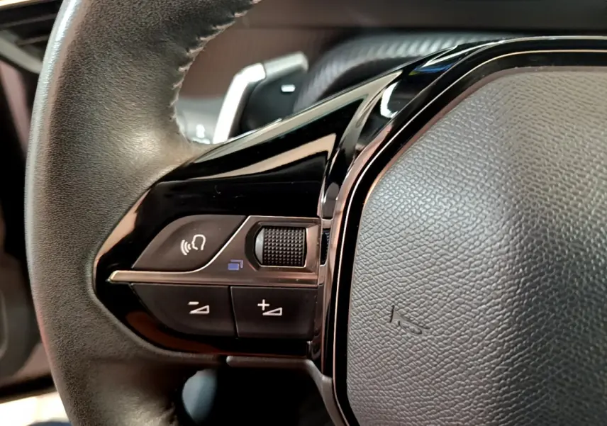 Gros plan sur les commandes vocales et volume du volant cuir noir du Peugeot 2008 gris clair 2021 PureTech.