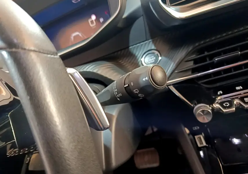 Gros plan sur la commande d’essuie-glace à gauche du volant cuir du Peugeot 2008 gris clair, tableau de bord moderne.