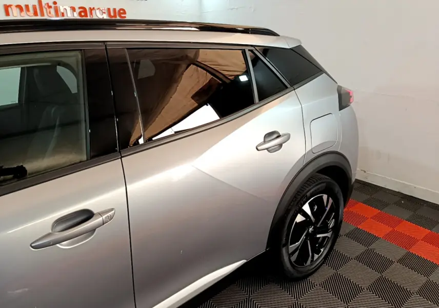 Profil arrière droit d'un Peugeot 2008 gris clair avec jantes noires et toit noir contrasté en intérieur showroom.