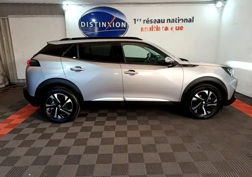 Peugeot 2008 gris clair vue de profil côté gauche, avec jantes noires et toit panoramique en intérieur showroom.