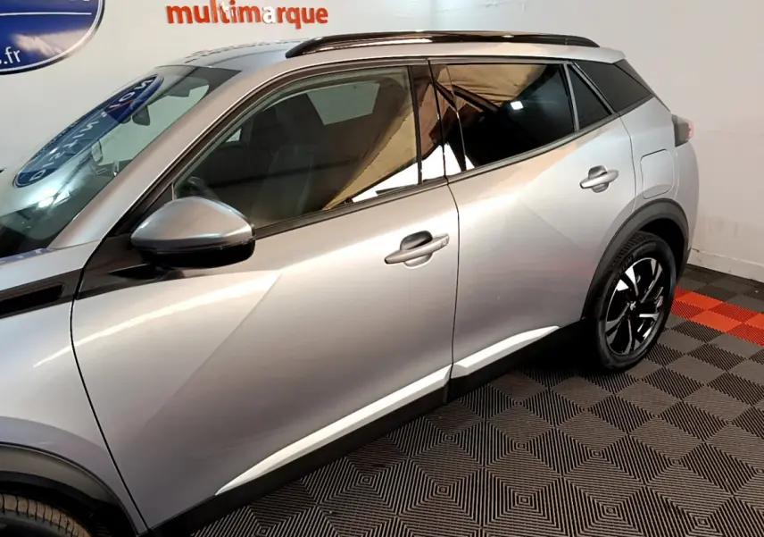 Profil côté gauche d'un Peugeot 2008 gris clair 2021 avec jantes noires et toit noir dans un showroom.