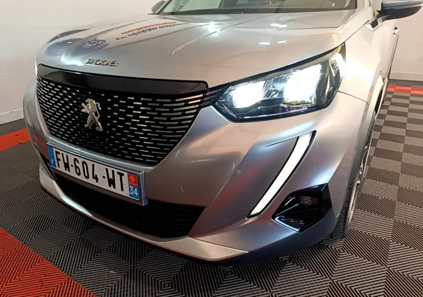Vue 3/4 avant droit d'un Peugeot 2008 gris clair avec phares LED allumés et calandre noire distinctive.