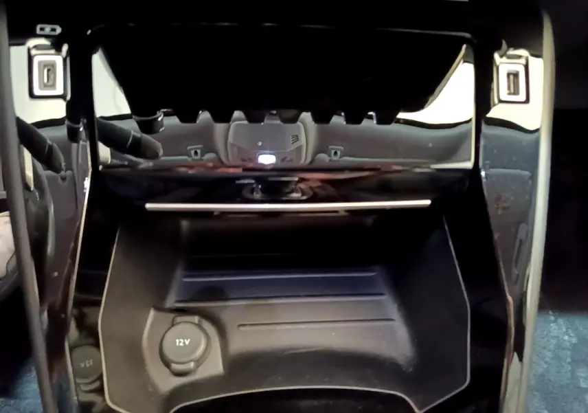 Prise 12V et rangement noir sous la console centrale du Peugeot 2008 gris clair, vue intérieure rapprochée.