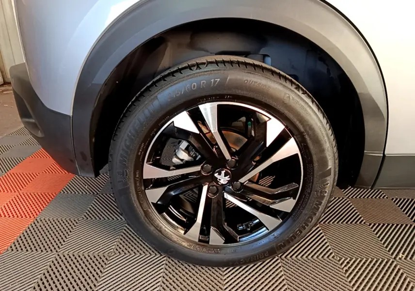 Gros plan sur la roue avant gauche du Peugeot 2008 gris clair, jante alliage noire et argentée au design moderne.