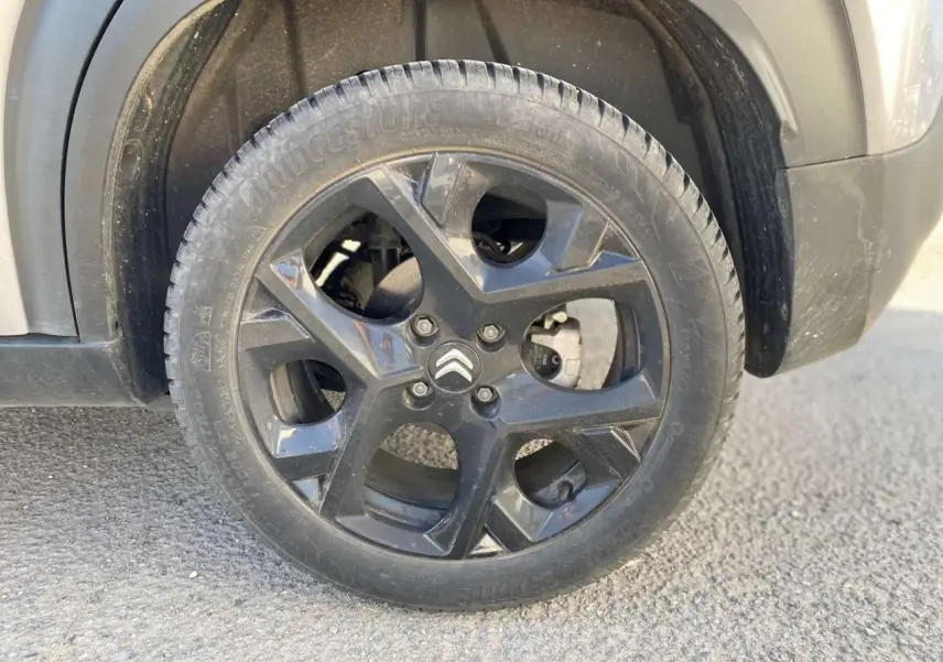 Gros plan sur la roue avant droite gris foncé d'un Citroën C3 Aircross 2024 avec jante noire et logo Citroën visible.