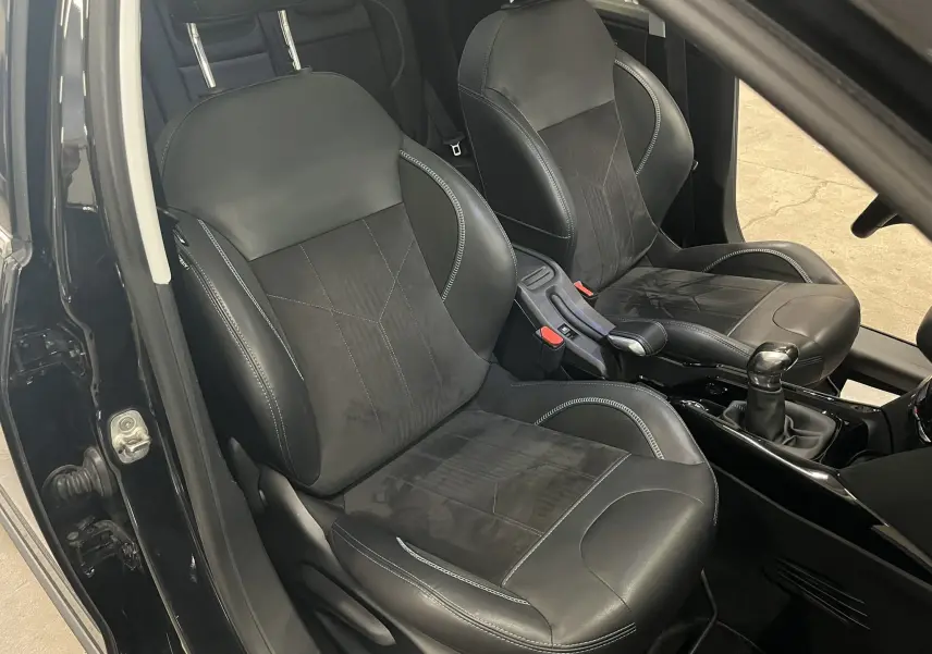 Vue intérieure côté conducteur montrant les sièges en cuir noir et la console centrale avec levier de vitesse manuelle.