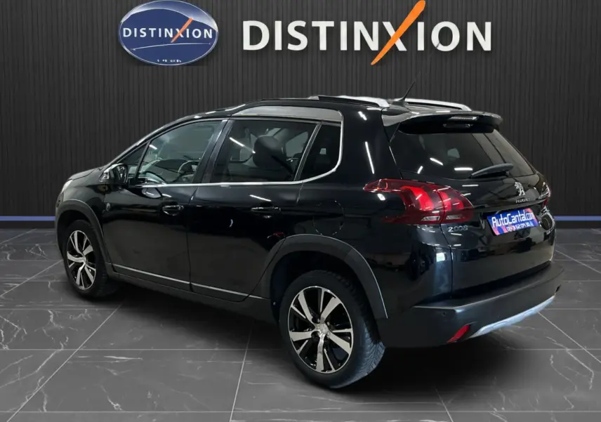 Peugeot 2008 noir vue 3/4 arrière droit, avec jantes alliage et barres de toit, stationnée en intérieur showroom.