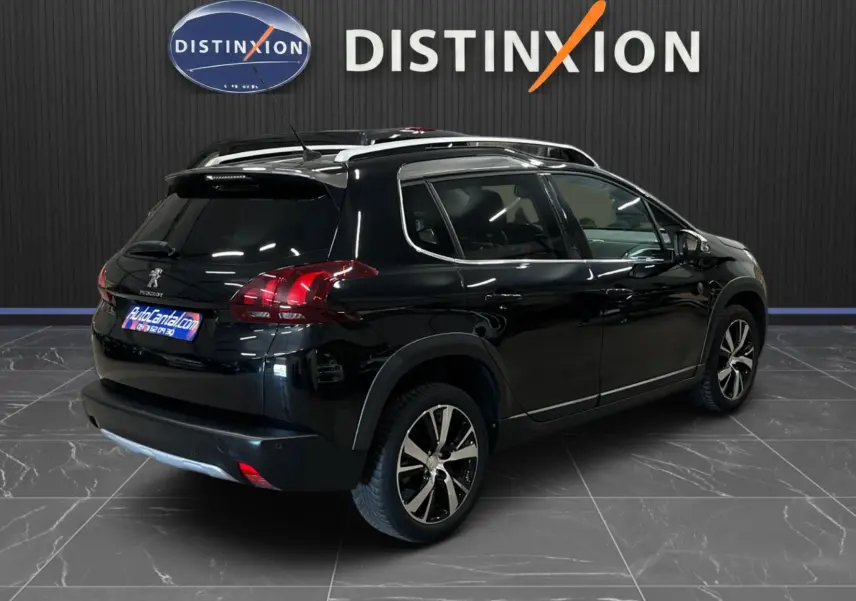 Vue 3/4 arrière droite d’un Peugeot 2008 noir avec jantes alliage et barres de toit, en intérieur showroom.