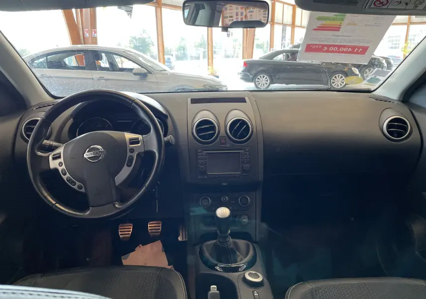 Intérieur noir du Nissan Qashqai 2013, vue frontale du tableau de bord avec volant multifonction et levier de vitesse manuel.