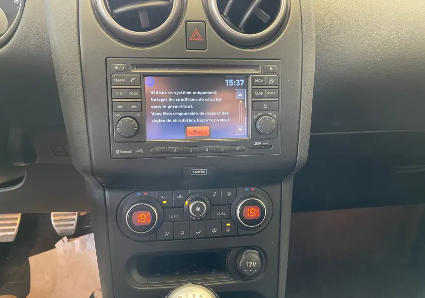 Tableau de bord du Nissan Qashqai 2013 avec écran central, commandes climatisation et levier de vitesse manuel visible.