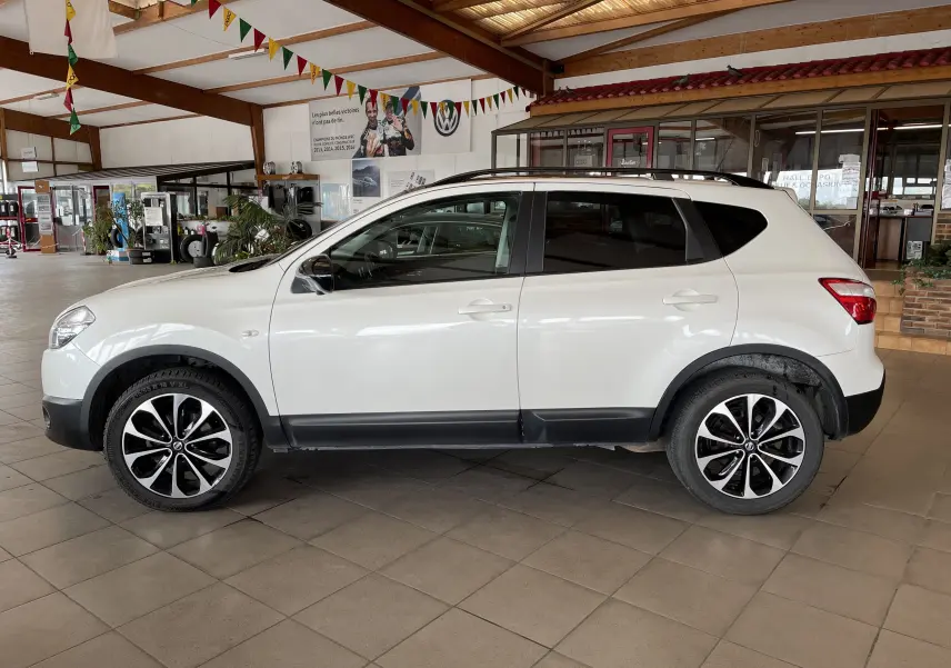 Profil côté gauche d'un Nissan Qashqai blanc 2013 avec jantes noires et blanches, garé en intérieur lumineux.