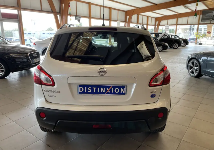 Vue arrière d'un Nissan Qashqai blanc 2013 dans un showroom, avec logo et plaques visibles.