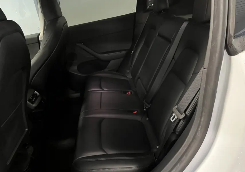 Vue côté droit des sièges arrière noirs en cuir du Tesla Model Y blanc 2022, avec ceintures de sécurité visibles.