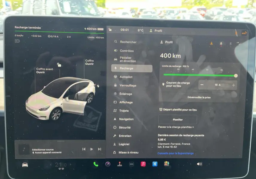 Écran tactile intérieur montrant l'interface de recharge d'une Tesla Model Y blanche en vue de face.