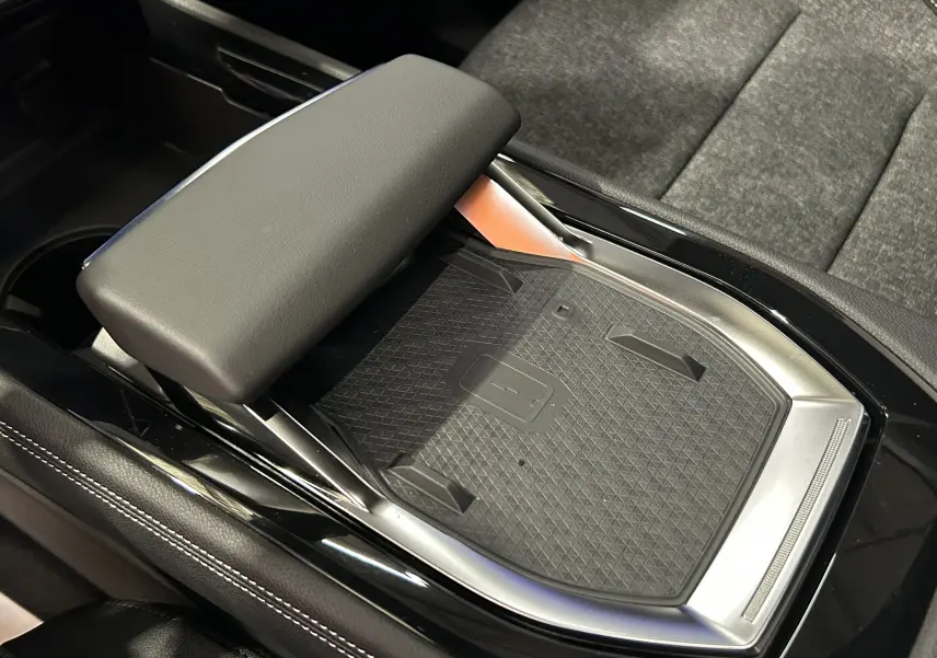 Gros plan sur la console centrale noire du Renault Austral Ph.2 E-TECH avec surface de charge sans fil et accoudoir rembourré.