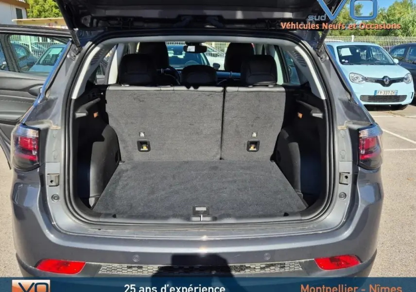 Coffre ouvert d'un Jeep Compass gris 3/4 arrière, montrant l'espace de chargement et les sièges arrière rabattables.