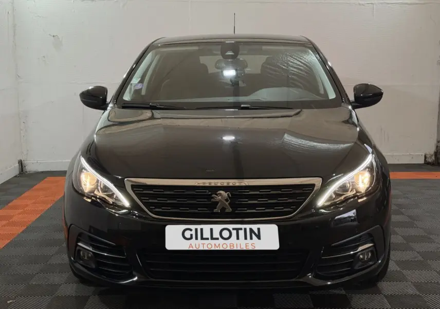 Vue frontale d'une Peugeot 308 noire avec phares allumés et calandre au lion distinctif.