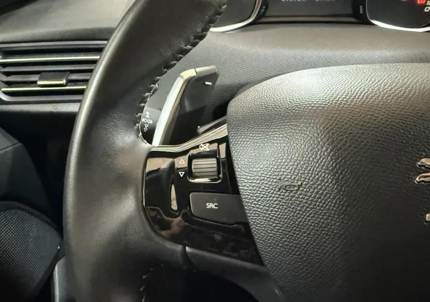 Gros plan sur le volant cuir noir de la Peugeot 308 Puretech 130, avec commandes audio intégrées côté gauche.