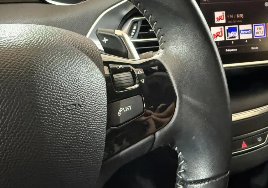 Gros plan sur le volant cuir noir de la Peugeot 308 2020 avec commandes intégrées et écran tactile en arrière-plan.