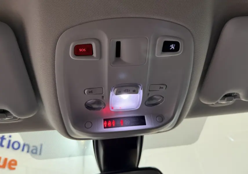 Vue en contre-plongée du plafonnier gris clair avec boutons SOS et logo Peugeot éclairés dans une Peugeot 308 noire.