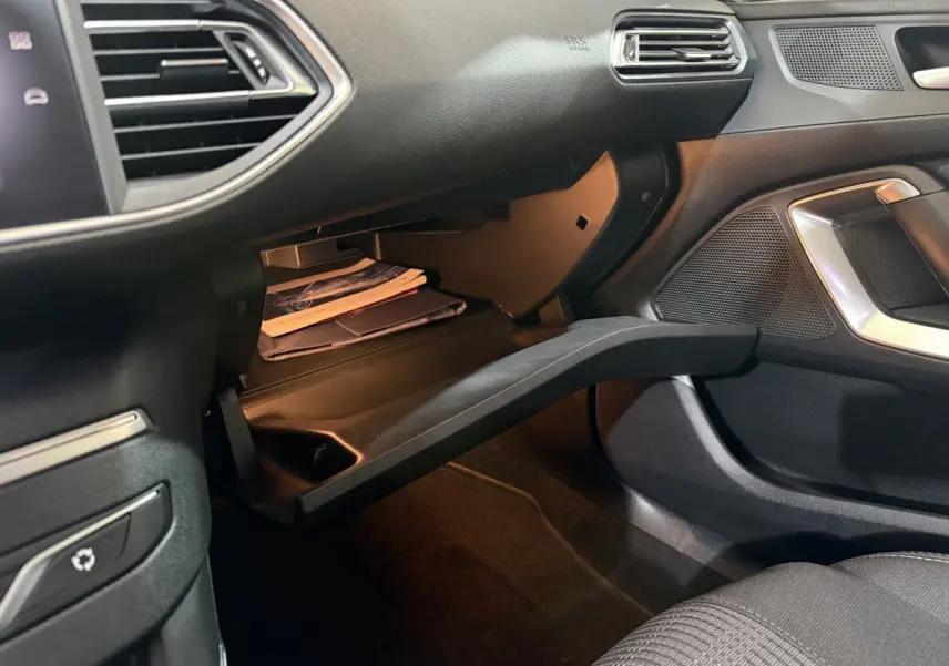 Intérieur côté passager d'une Peugeot 308 noire, boîte à gants ouverte avec documents visibles.