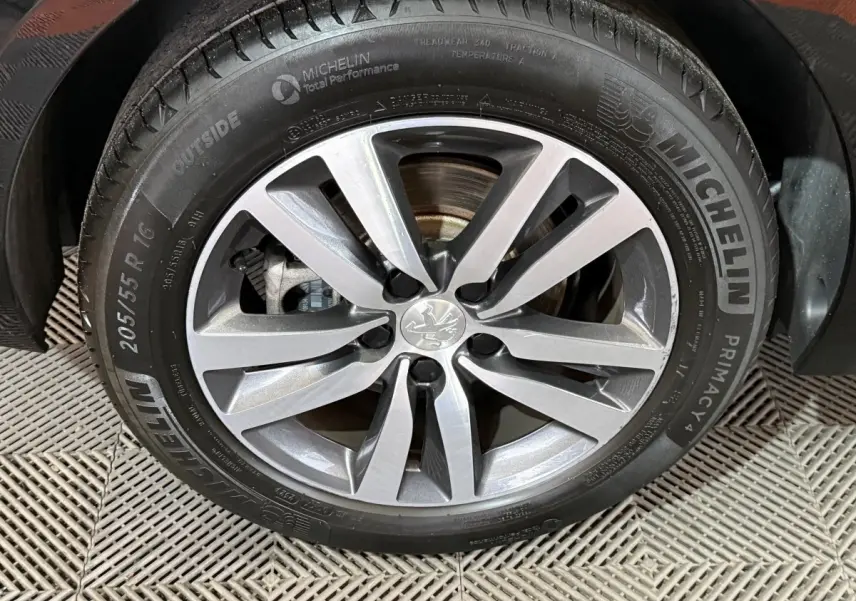 Gros plan sur la roue avant droite de la Peugeot 308 noire, mettant en valeur la jante alliage et le pneu Michelin.