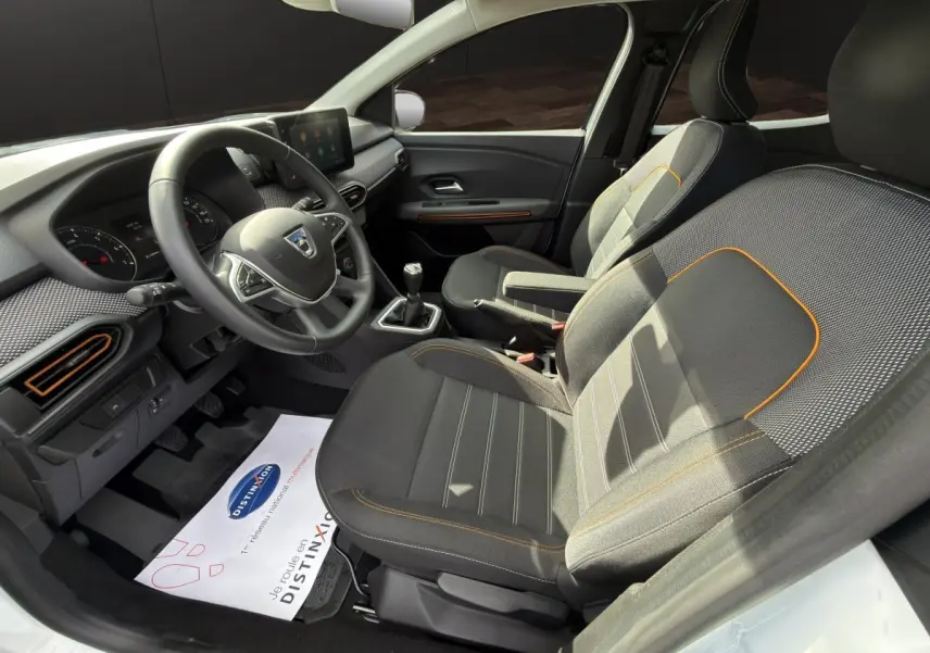 Vue intérieure côté conducteur de la Dacia Sandero Stepway 2022, sièges tissu noir avec surpiqûres orange et volant multifonctions.