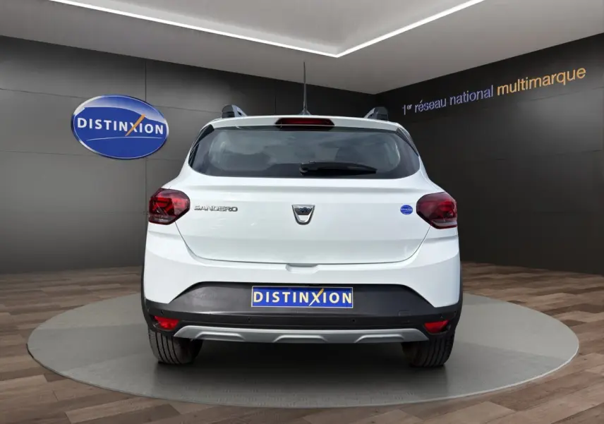 Vue arrière d'une Dacia Sandero Stepway blanche 2022 dans un showroom avec logo Distinxion en arrière-plan.