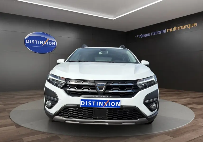 Vue de face d'une Dacia Sandero Stepway blanche avec calandre noire et phares LED dans un showroom.