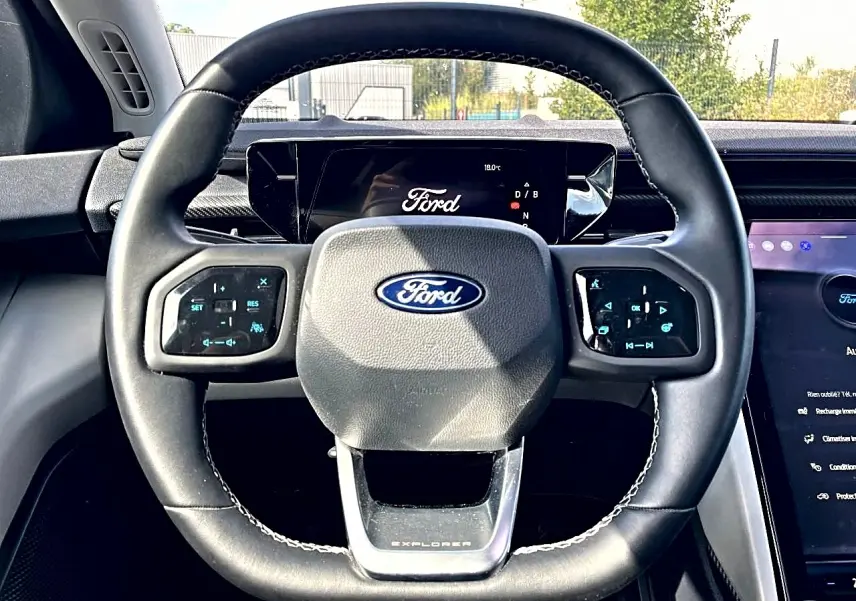 Vue rapprochée du volant noir du Ford Explorer 2025 avec commandes tactiles et logo Ford central visible.