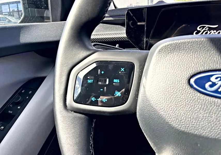 Gros plan sur le volant gris du Ford Explorer 2025 avec commandes multifonctions et logo Ford visible.