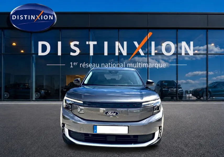 Vue frontale d'un Ford Explorer électrique gris métallisé garé devant une vitrine avec logo Distinxion.