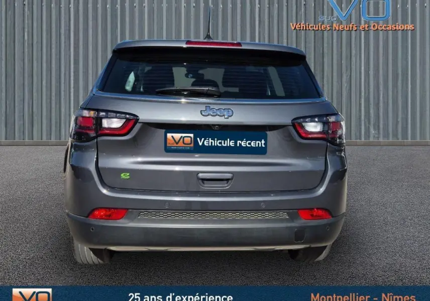 Vue arrière d'un Jeep Compass gris 2024 avec feux LED et logo e-Hybrid visible sur un parking.