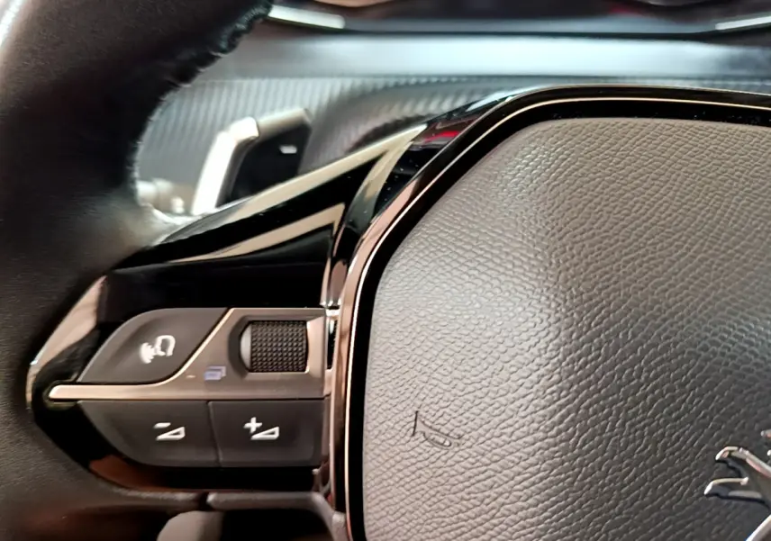 Gros plan sur les commandes gauche du volant cuir noir du Peugeot 2008 gris foncé version Allure 2022.