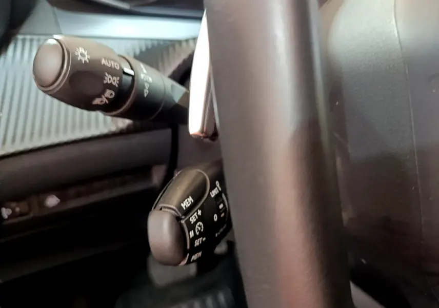 Gros plan sur les commandes au volant cuir noir du Peugeot 2008 2022, avec levier de clignotant et régulateur de vitesse.