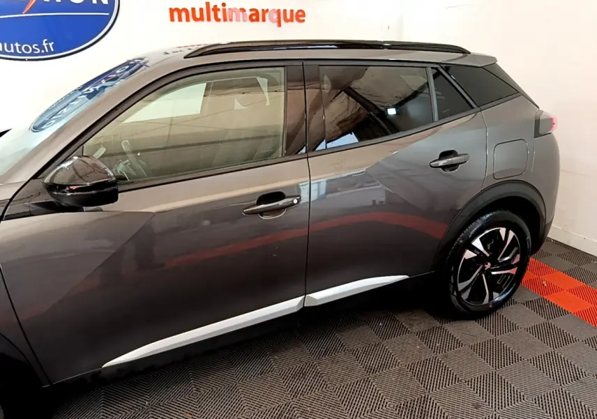 Profil droit d'un Peugeot 2008 gris foncé avec jantes noires et toit noir en intérieur showroom.