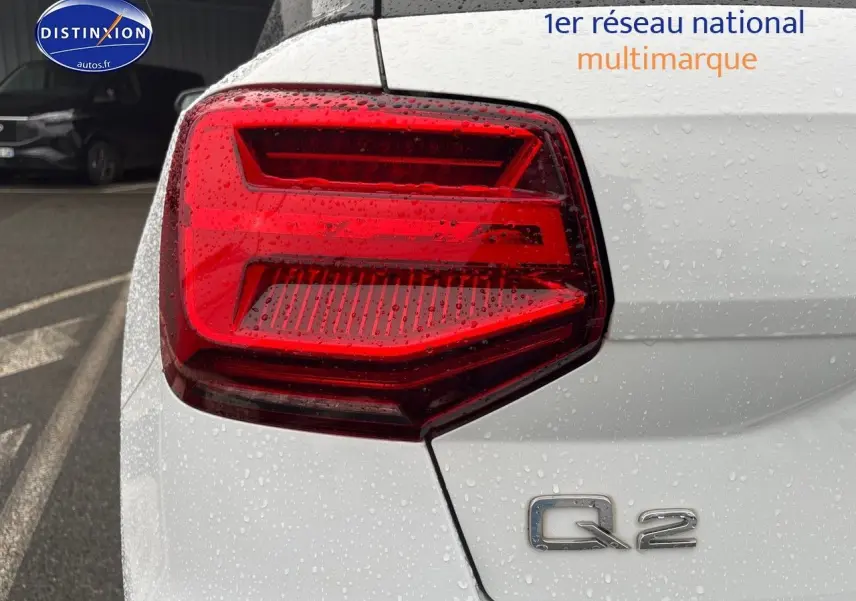 Gros plan sur le feu arrière gauche et le logo Q2 d’un Audi Q2 blanc Ibis sous la pluie.