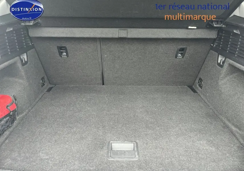 Coffre spacieux de l'Audi Q2 blanc Ibis, vue intérieure arrière avec tapis gris et filet de rangement rouge sur le côté.
