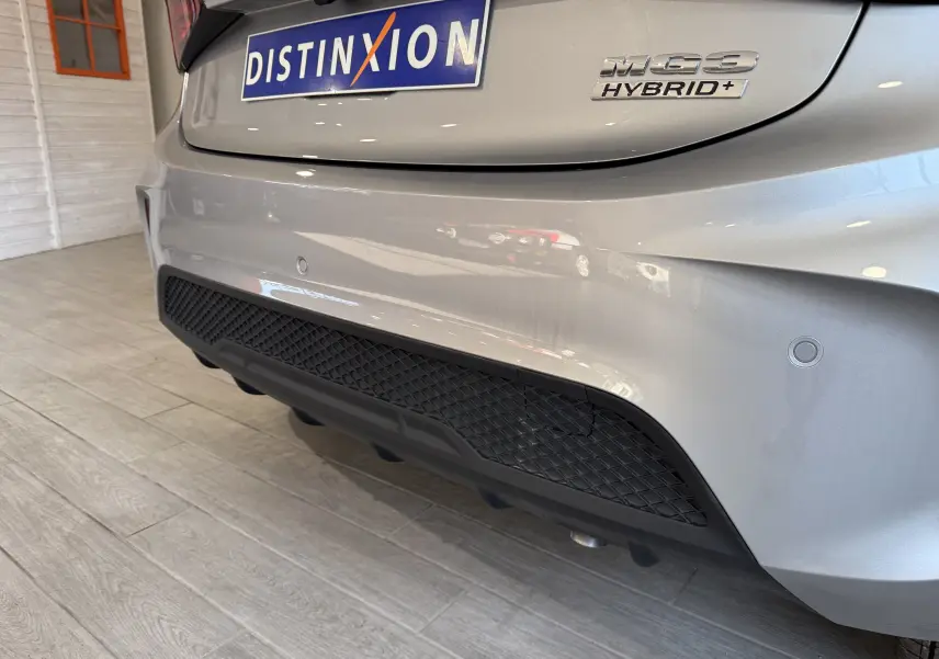Gros plan sur l’arrière droit du MG3 Cosmic Silver 1.5 L Hybrid+ avec logo et diffuseur noir en intérieur showroom.