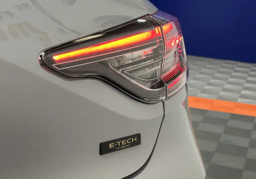 Gros plan sur le feu arrière droit allumé d’une Renault Clio V gris Rafale Métal avec badge E-TECH Hybrid.
