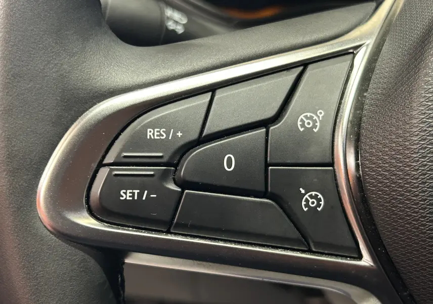 Gros plan sur les commandes de régulateur de vitesse au volant d'une Renault Clio V gris Rafale métal.